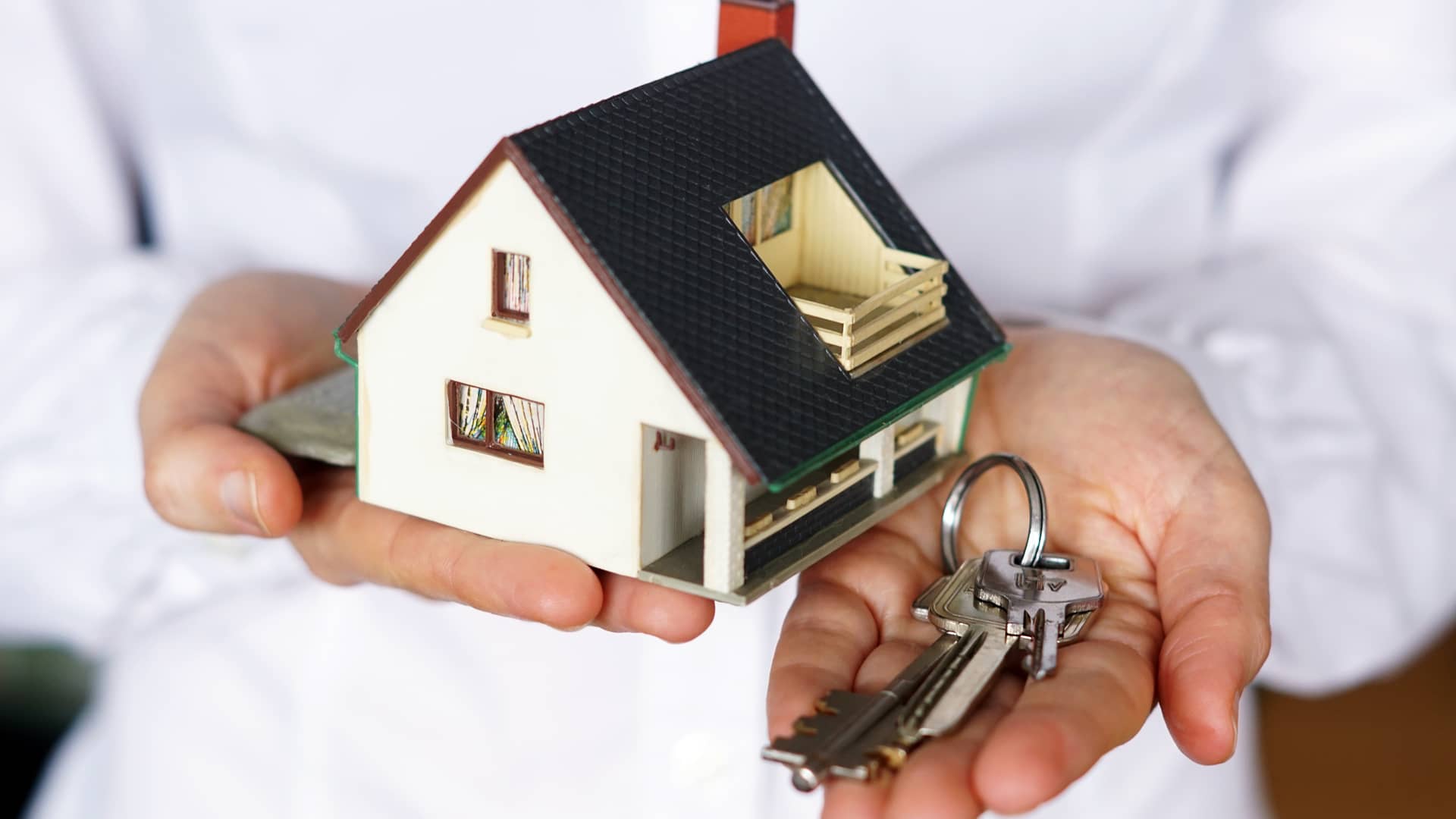 Persona sujeta una maqueta de una casa mientras entrega las llaves de una casa que ha vendido recientemente simbolizando el impuesto de plusvalía