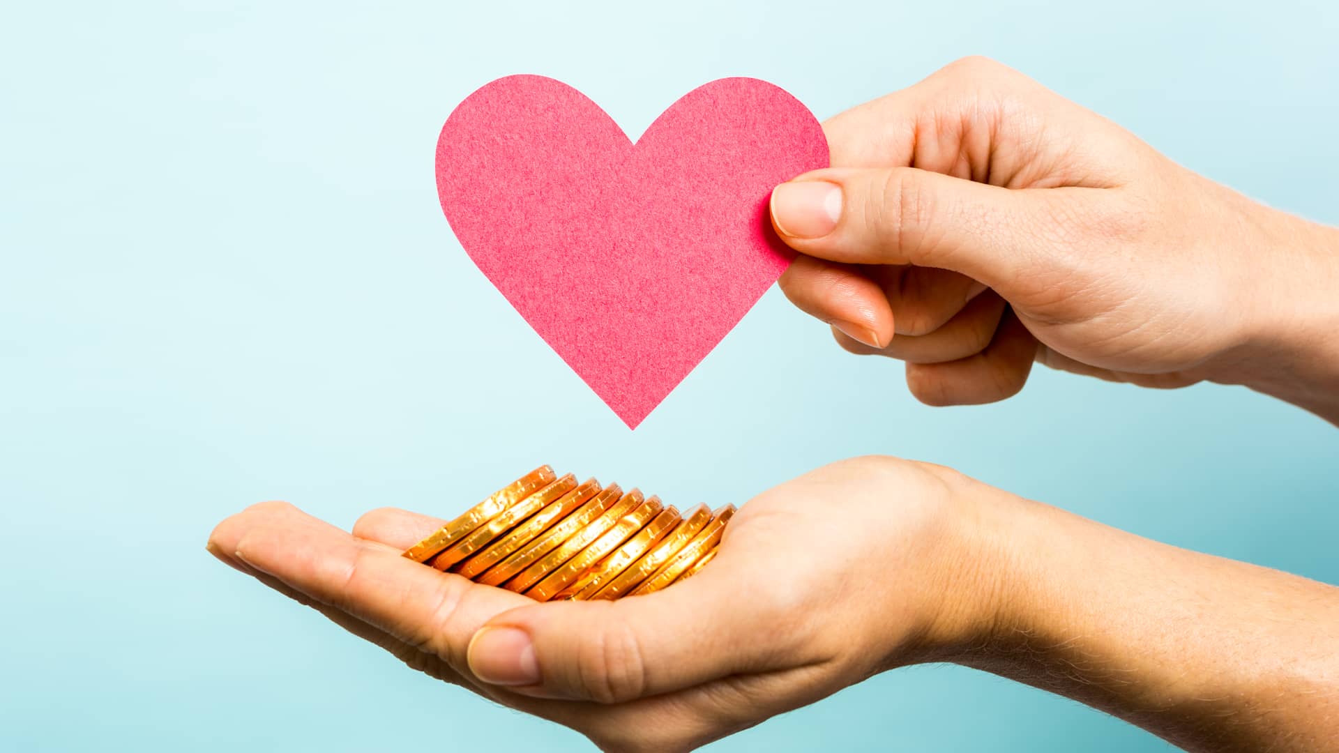 Persona con mano extendida ofreciendo monedas de chocolate mientras sostiene la silueta de un corazón de cartulina símboliza el crowdfunding de donación