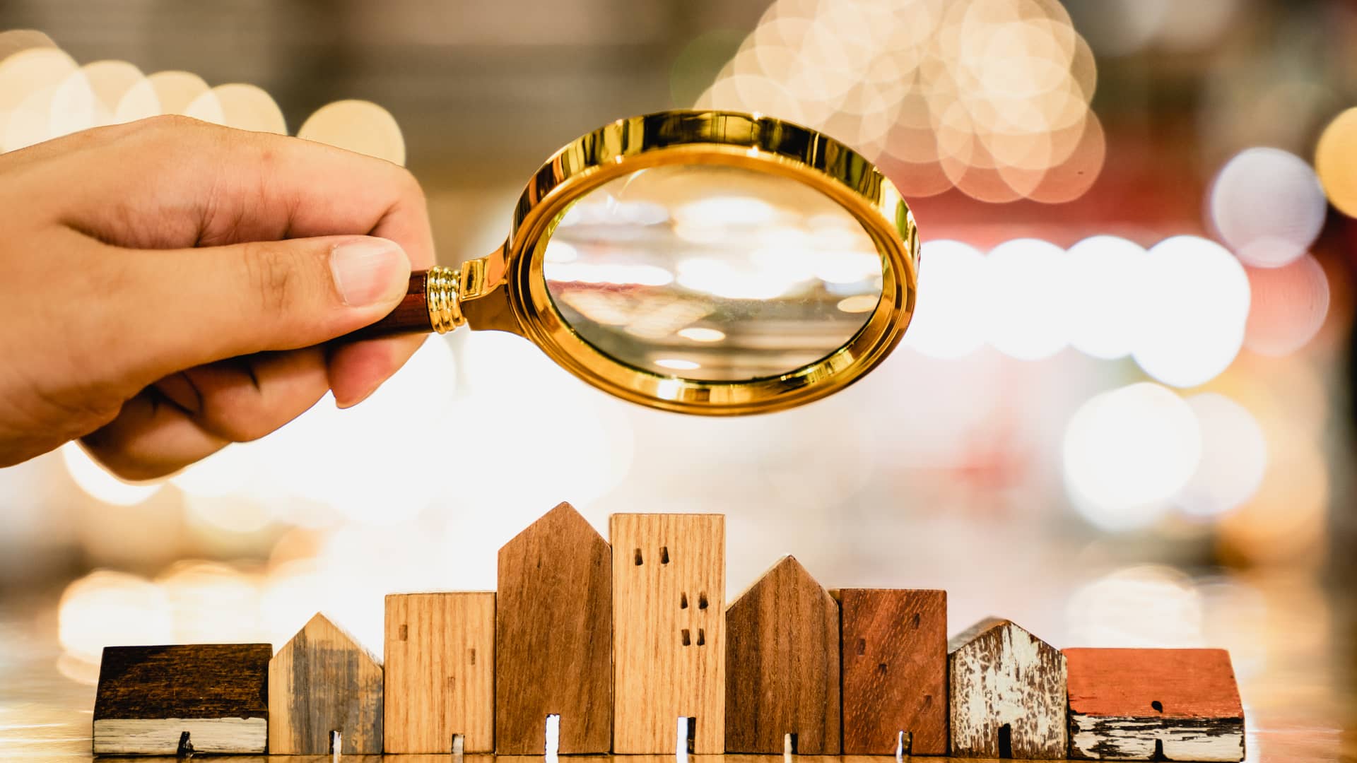 Persona con lupa observa pequeñas casitas de madera representando a una persona que analiza las posibilidades del mercado del crowdfunding inmobiliario