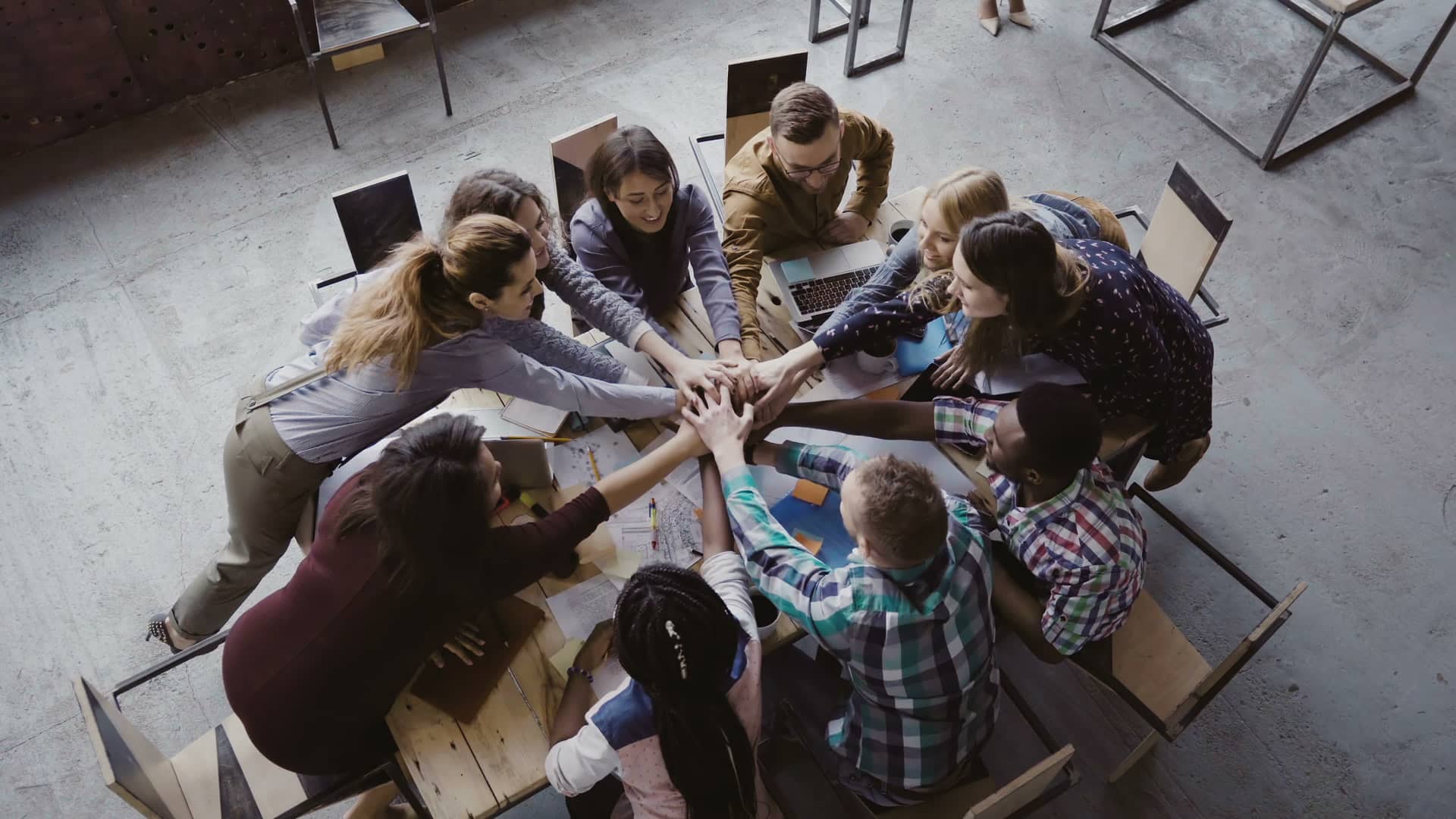Varias personas sentadas en círculo poniendo la mano en el centro a modo de "todos a una" símbolizando las distintas plataformas de crowdfunding