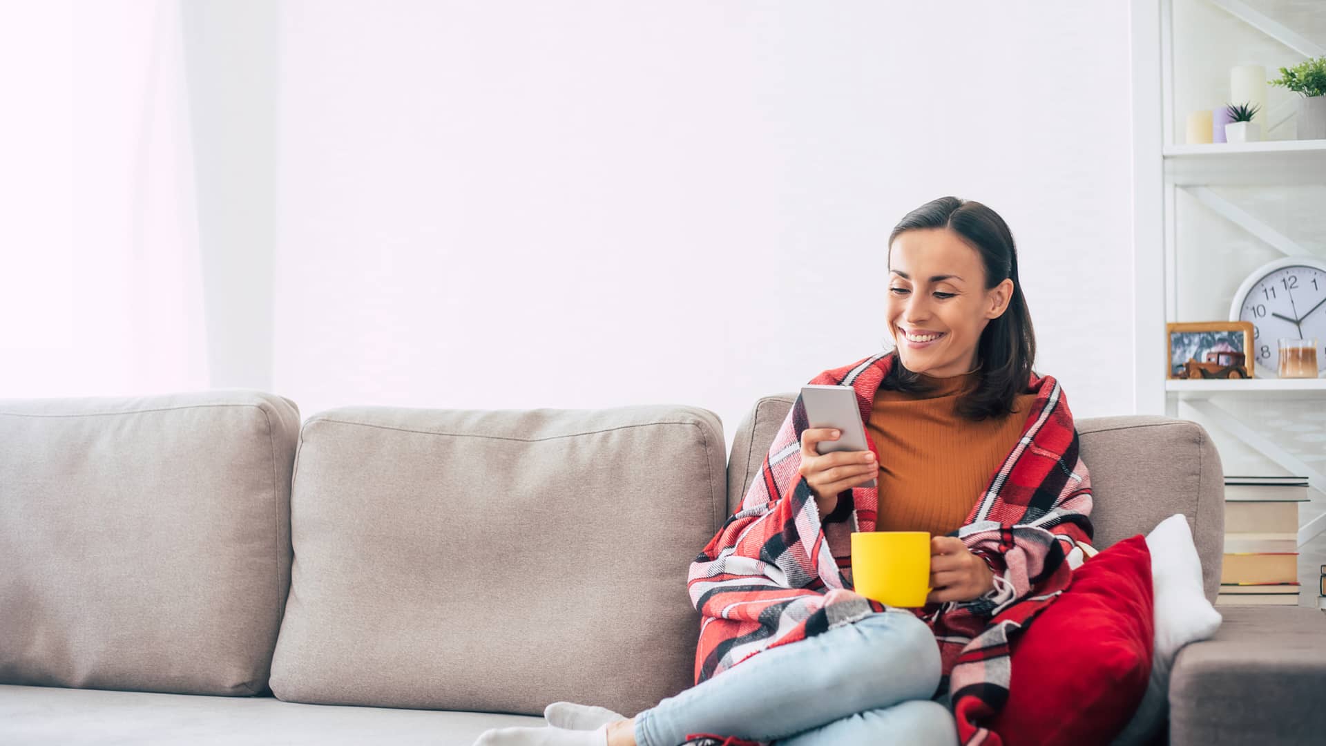Mujer sentada en su sofá de casa realizando un bizum a su amiga con su smartphone