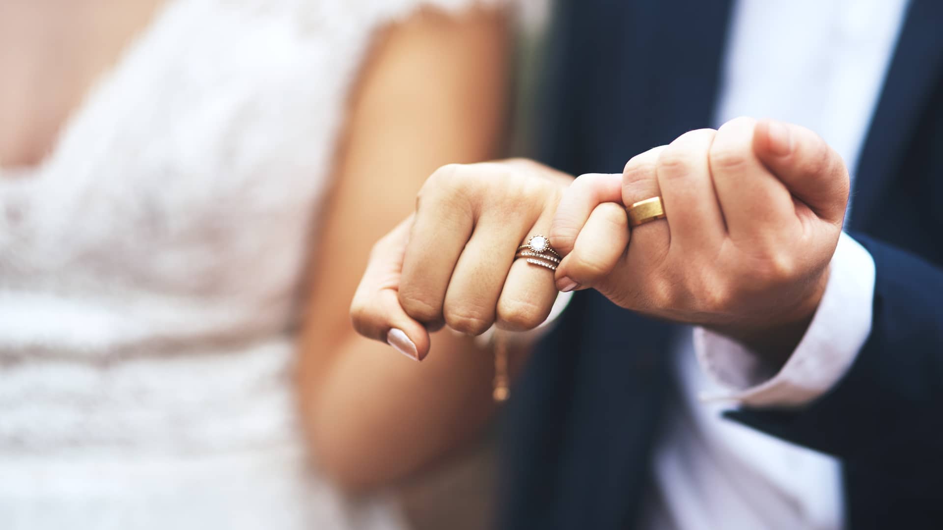 Pareja de recien casados muestran sus manos entrelazadas con sus nuevas alianzas, representando su nueva vida en pareja y su hipoteca compartida