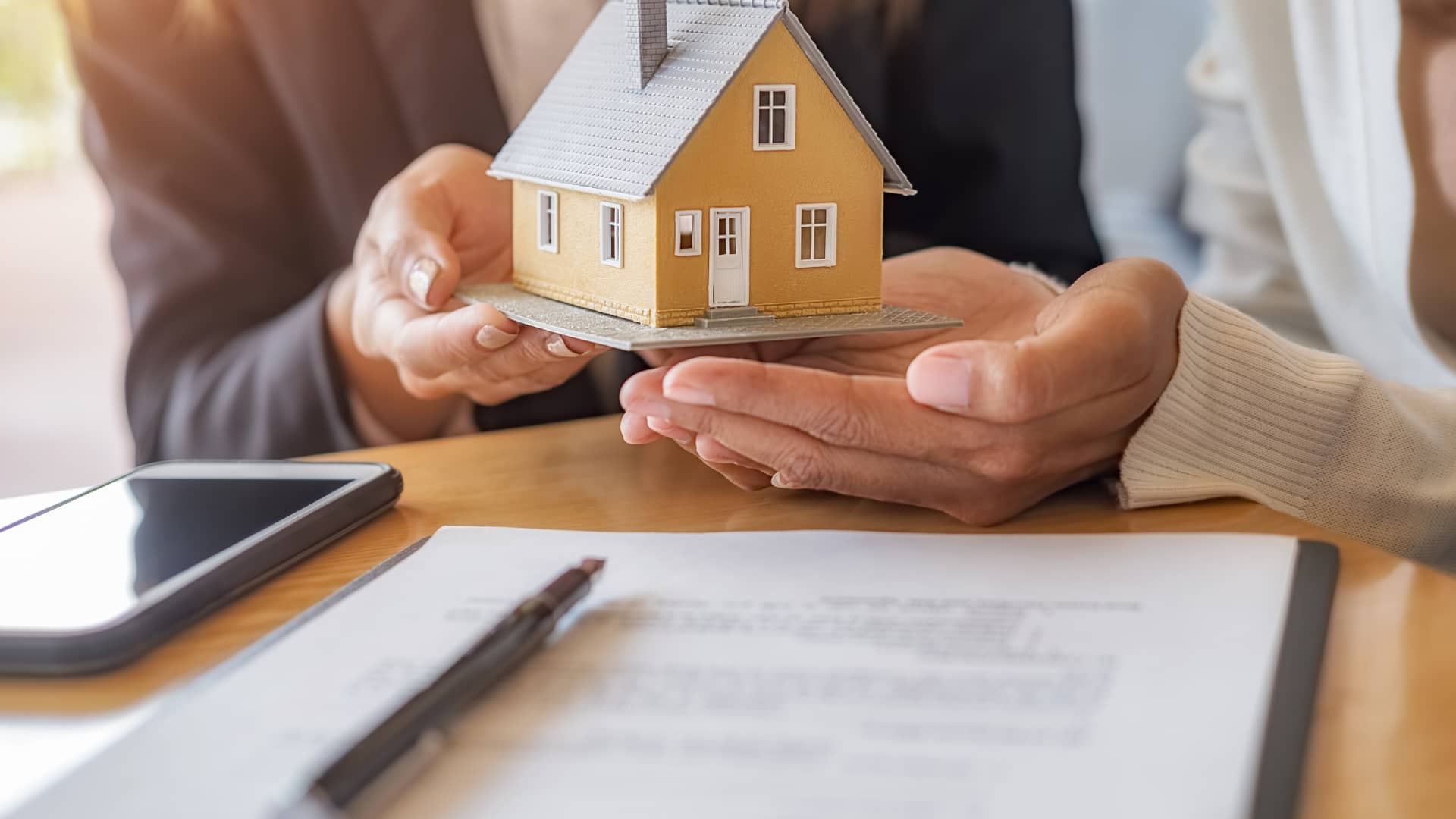 Una persona le entrega a otra una maqueta de una casa, sobre un contrato, representando las hipotecas entre particulares