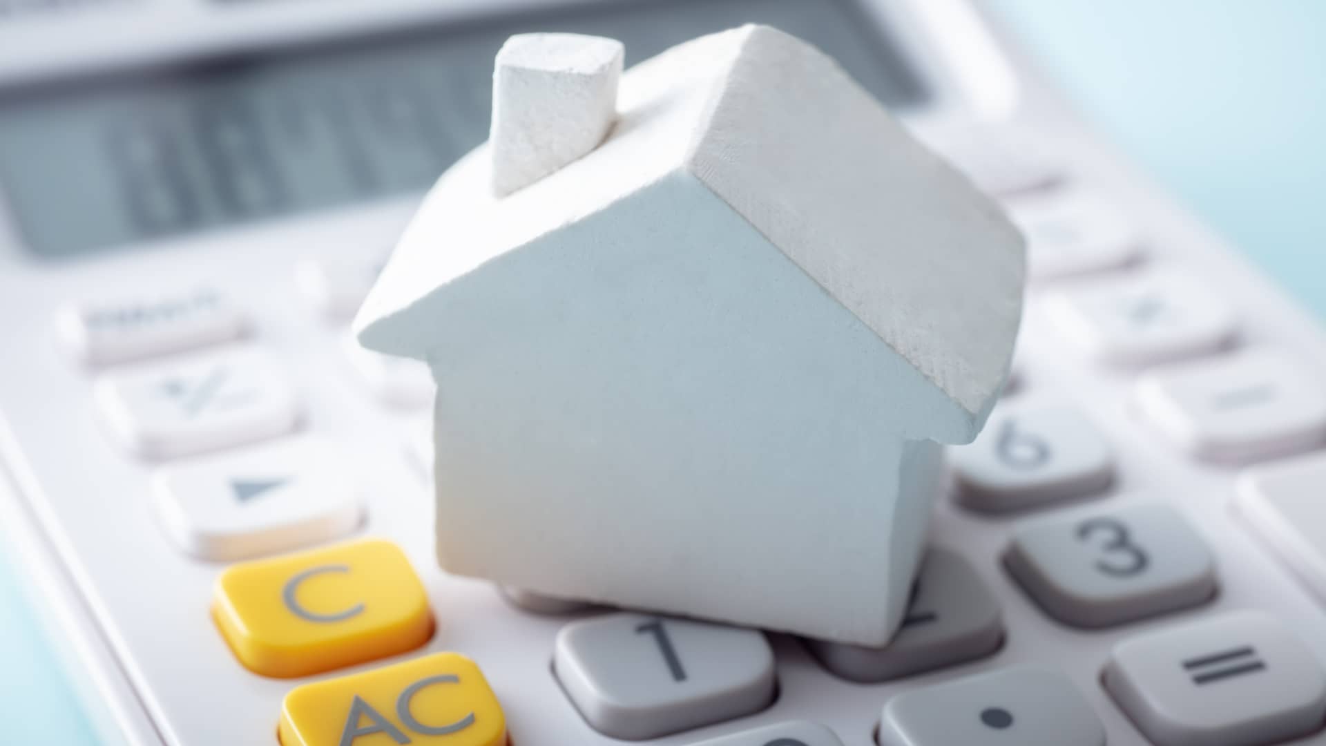 Casita blanca de madera sobre una calculadora representa el cálculo del primer pago de la hipoteca