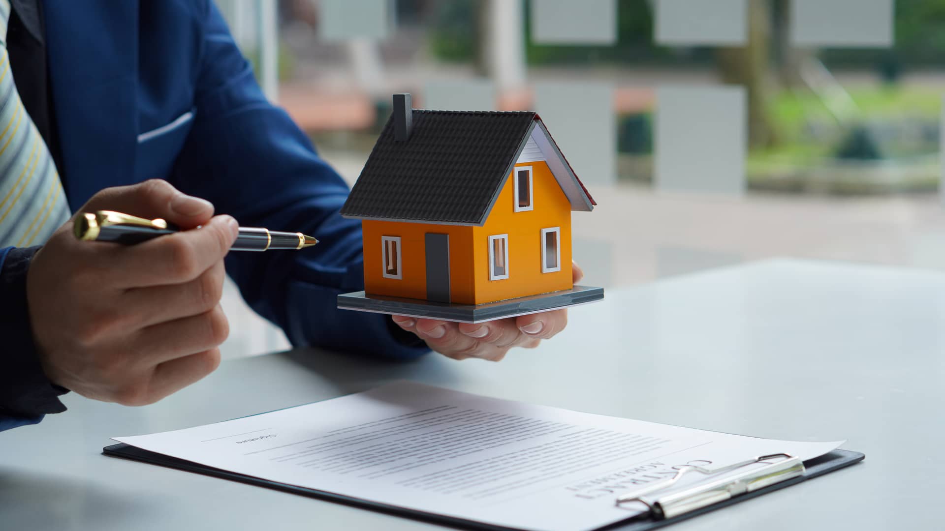 Persona a punto de firmar una hipoteca que ha conseguido pese a no tener contrato fijo, sostiene una maqueta de una casa