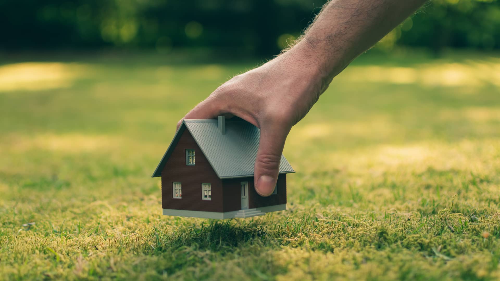 Persona colocando la maqueta de una casa sobre un terreno, representando la posiblidad de solicitar una hipoteca para comprar el terreno sobre el que edificar