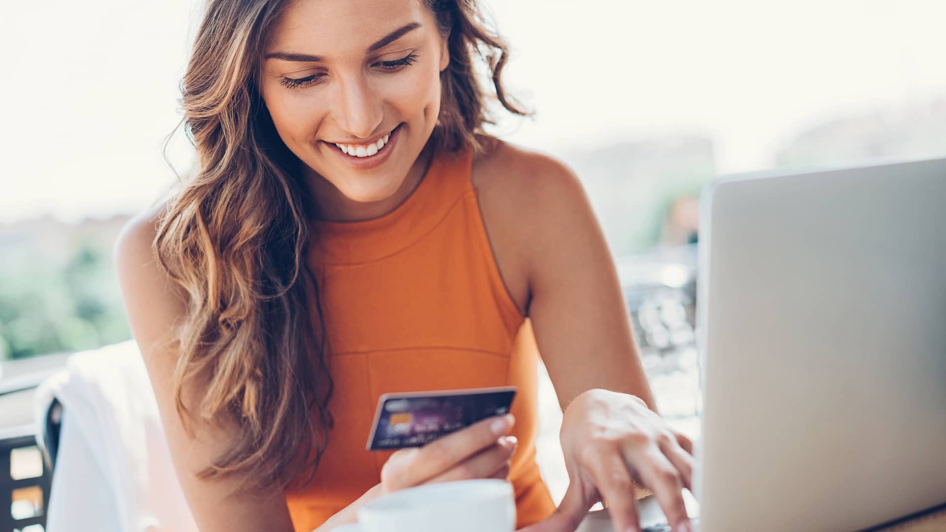 Mujer sonriente con tarjeta de crédito y ordenador portátil representa tarjetas comprar internet